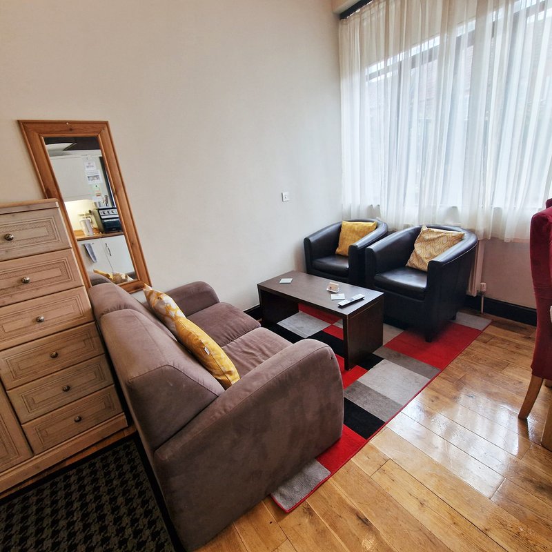 Living room with brown armchair, black sofa, wooden dresser, mirror, and red area rug
