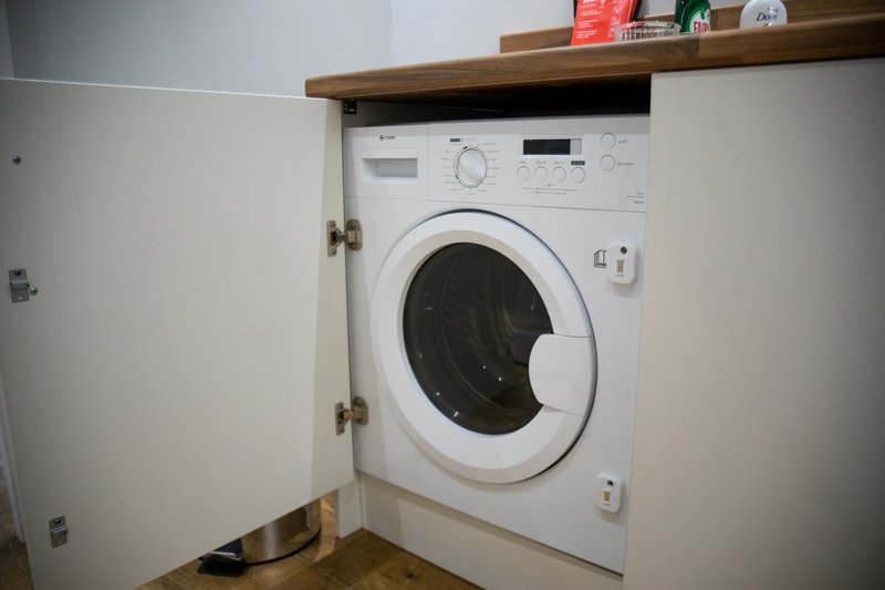 White integrated washing machine in fitted kitchen cupboard with wooden shelf above