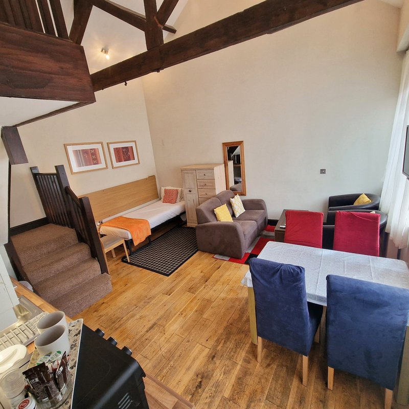 Open-plan studio with bed, sofa seating, wooden beams, and wooden flooring
