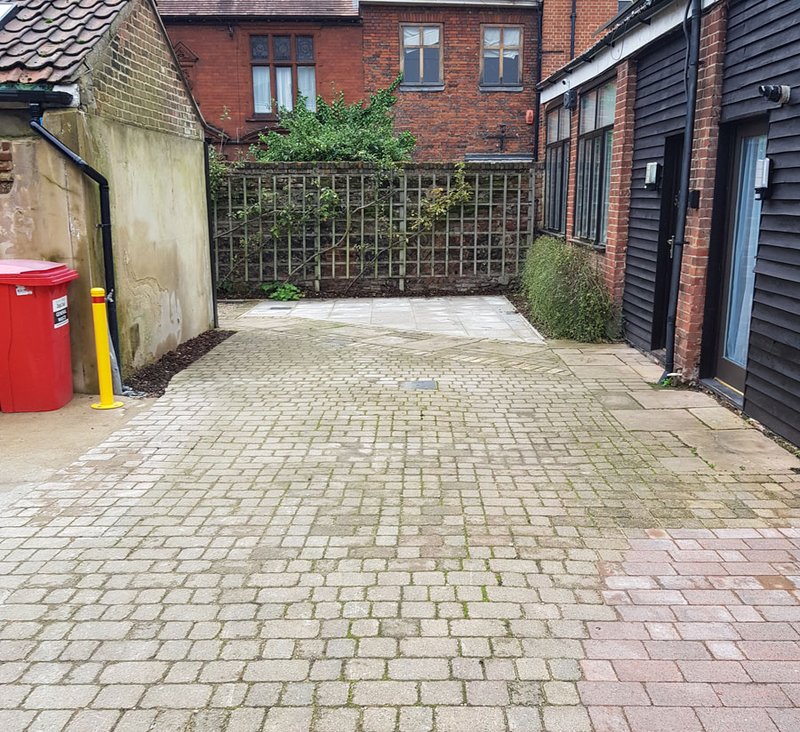 Paved driveway with brick buildings, metal gate, and red postbox