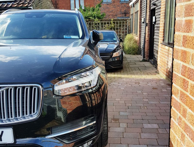 Driveway with two parked cars beside brick buildings and paved pathway