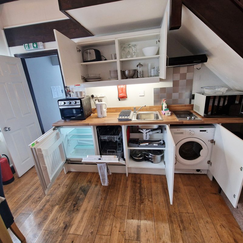 Compact kitchen with white cabinetry, wooden worktops, open storage and integrated appliances