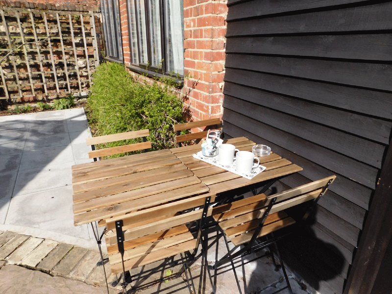 Wooden outdoor table and benches in paved garden area between brick and black cladding