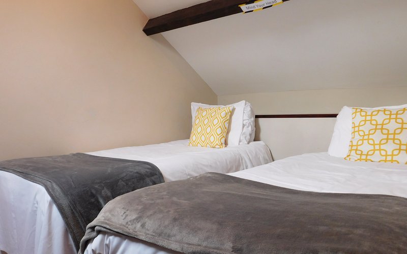 Twin bedroom with white bedding, gray throws, yellow patterned pillows, and exposed beam