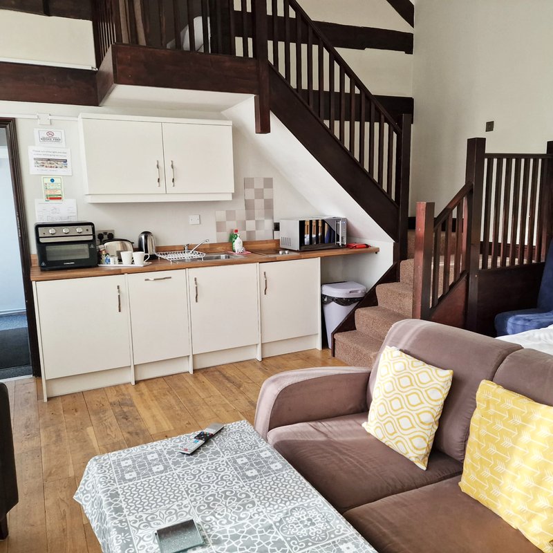 Open-plan kitchen and living area with stairs, brown sofa, kitchenette and wooden flooring