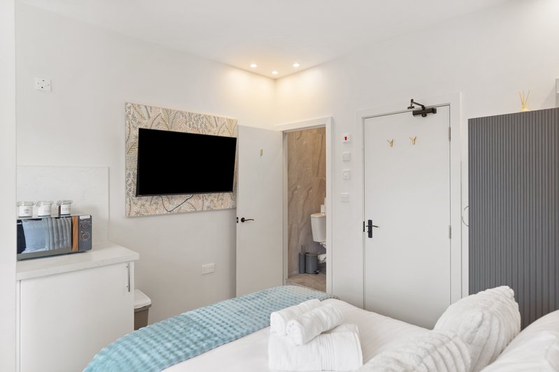 Compact bedroom with double bed, wall-mounted TV, white furniture and neutral décor