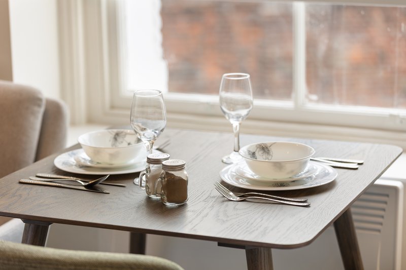 Dining table set for two with place settings, glasses, and window view