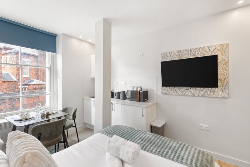 Modern bedroom with double bed, wall-mounted TV, desk, and large window overlooking brick building