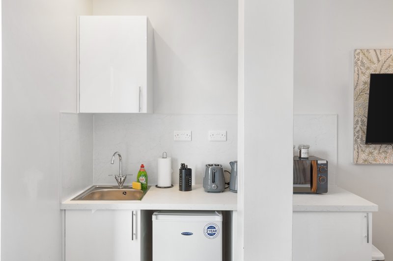 Compact kitchenette with white cabinetry, small sink, mirror cabinet and appliances