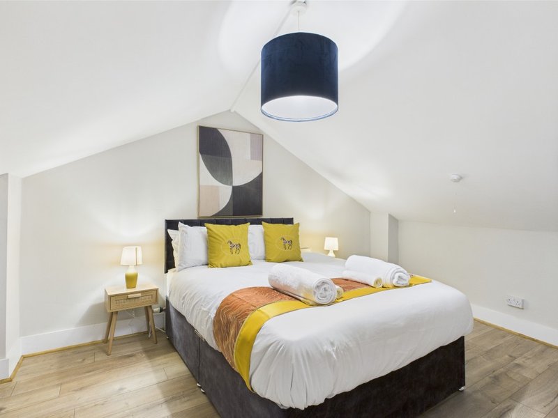 Bright bedroom with double bed, yellow cushions, wooden floor and pendant light