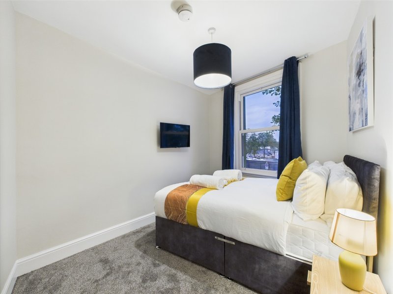 Modern bedroom with double bed, yellow and grey cushions, pendant lamp and window view