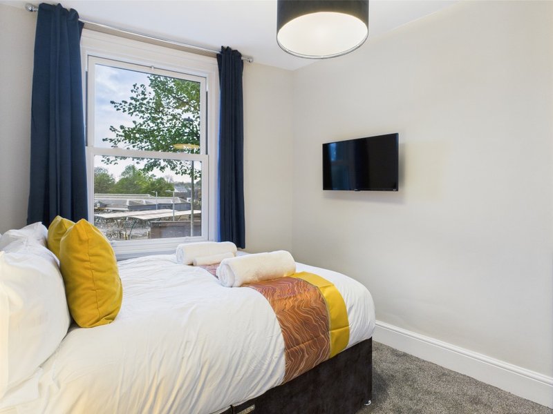 Modern bedroom with double bed, yellow cushions, wall-mounted TV and garden view