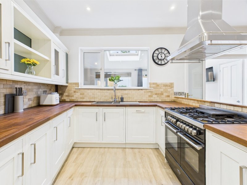 Modern kitchen with white cabinetry, wooden countertops, gas range, and yellow flowers on counter