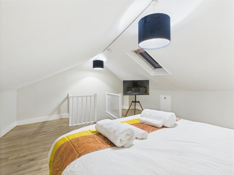 Attic bedroom with two single beds, white walls, wooden floor and ceiling lamp