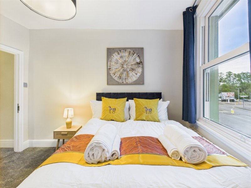 Bright bedroom with double bed, yellow and white bedding, bedside lamp, and large window