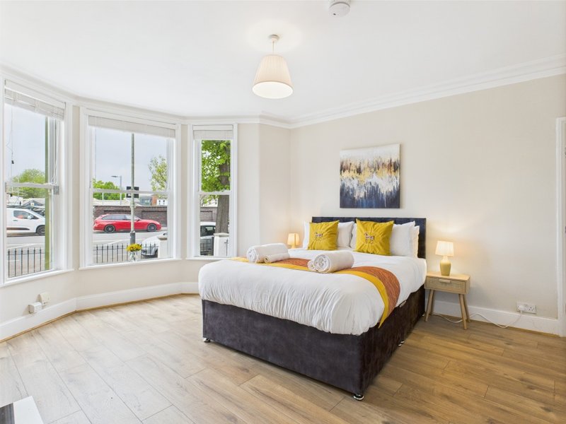 Bright bedroom with double bed, yellow and grey cushions, wooden floor and bay windows