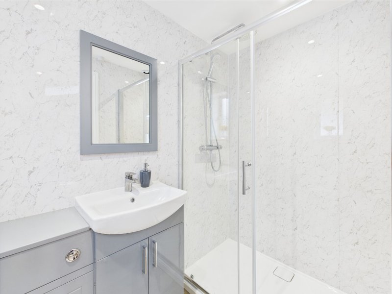 Modern bathroom with white marble tiles, grey vanity unit, mirror and glass shower enclosure