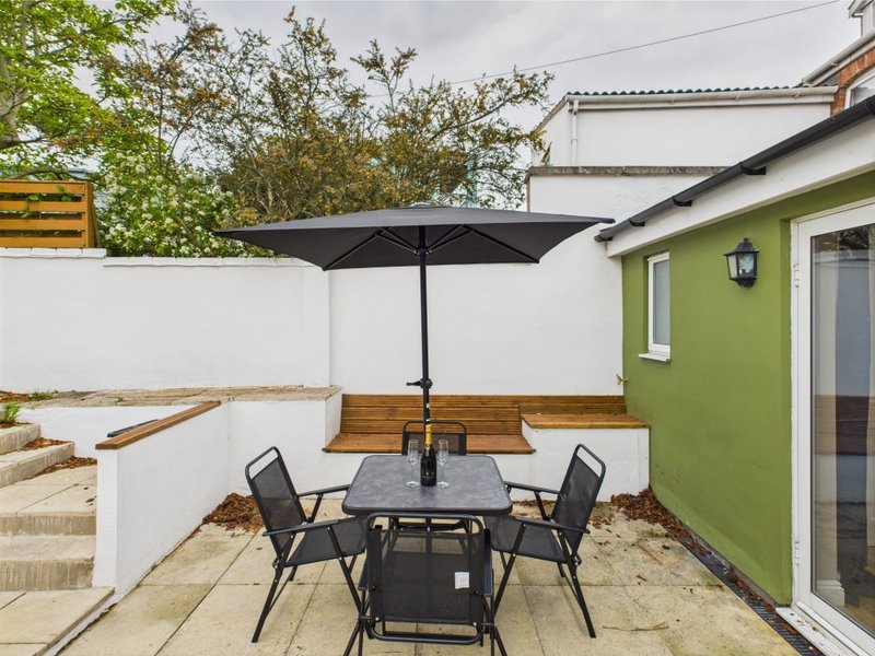 Patio area with dining table, black umbrella, chairs and green-walled house