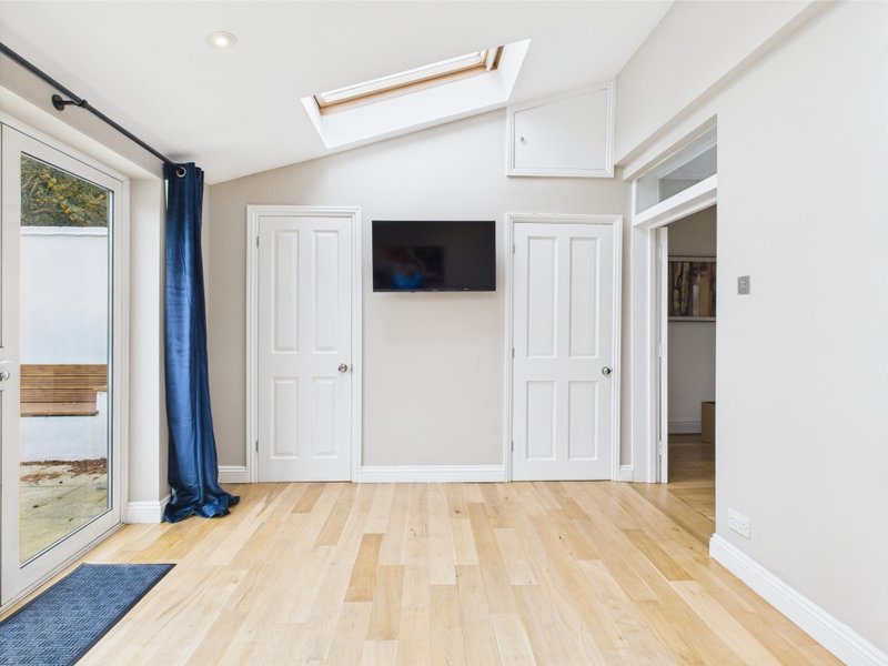 Bright modern bedroom with wooden flooring, wall-mounted TV, skylight and glass door to garden