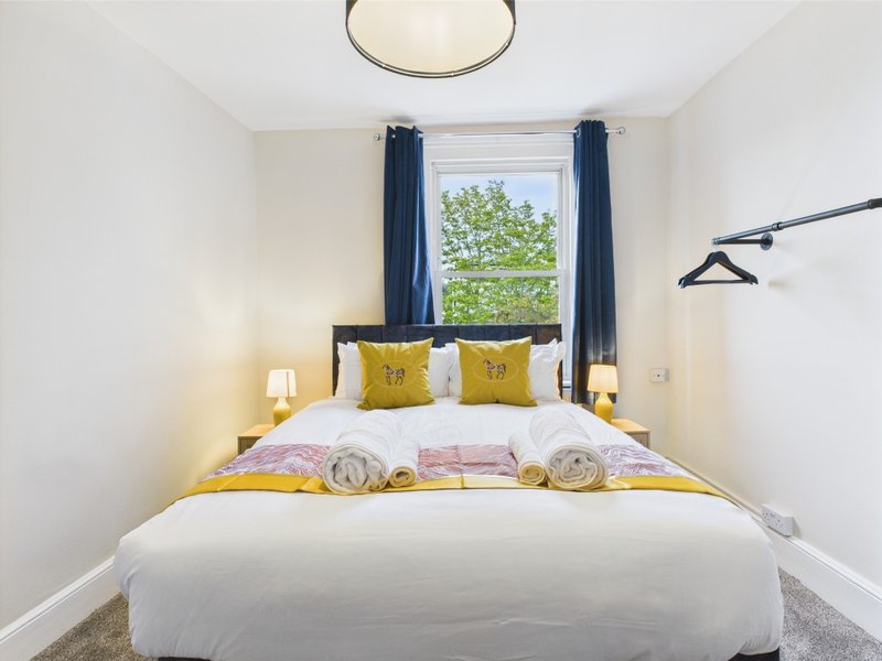 Modern bedroom with double bed, yellow cushions, white bedding, dark curtains and pendant light