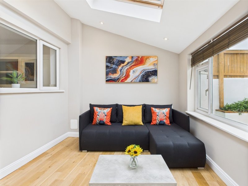 Modern living room with black corner sofa, colorful cushions, wooden floor and skylight