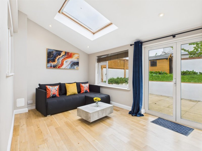 Bright living room with black sofa, orange and yellow cushions, wooden flooring, skylight and garden view