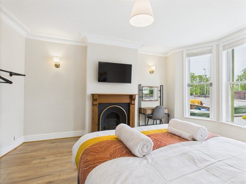 Bright bedroom with double bed, fireplace, wall-mounted TV and garden views through large windows