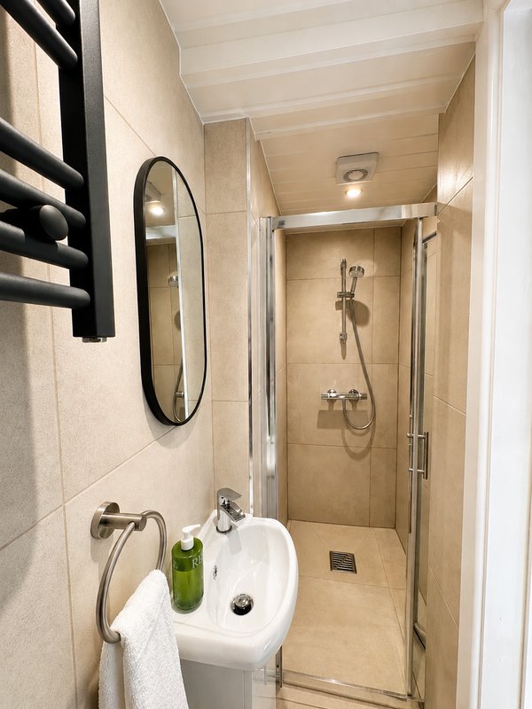 Modern bathroom with white sink, oval mirror, enclosed shower cubicle and tiled walls