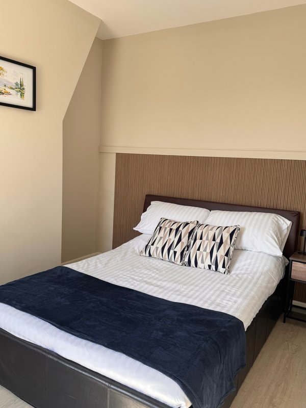 Bedroom with double bed, dark headboard, striped cushion, navy throw and white bedding