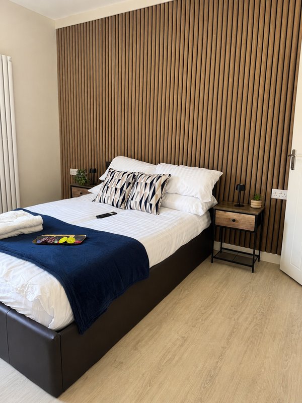 Modern bedroom with double bed, navy throw, striped cushions, wooden wall paneling, and wooden flooring
