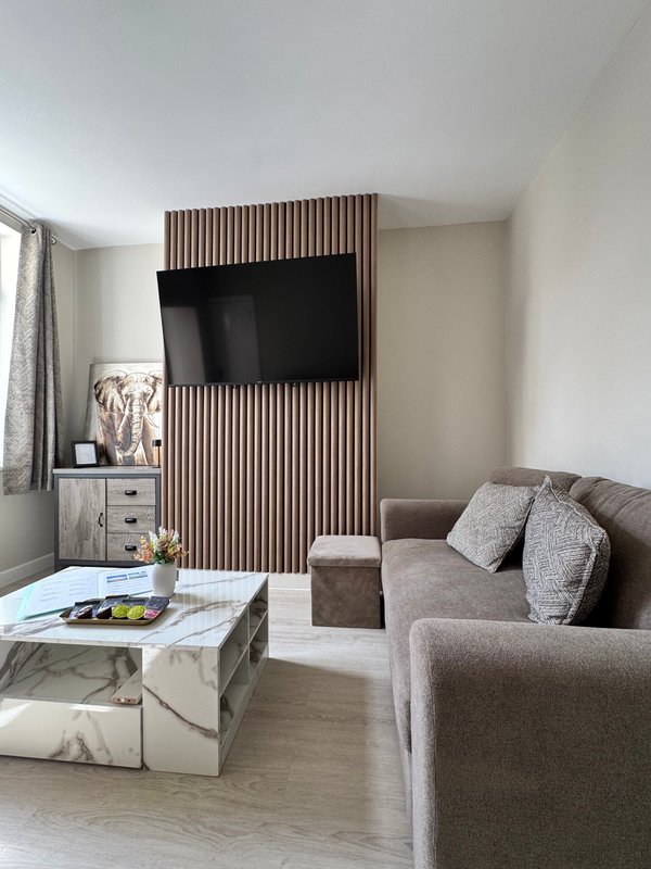 Modern living room with grey sofa, wall-mounted TV, marble coffee table and wooden accent wall
