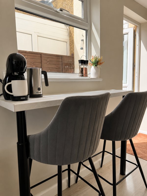 Modern kitchen counter with black bar stools, coffee maker, and window overlooking garden