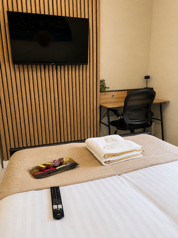 Modern bedroom with double bed, wall-mounted TV, wooden slat accent wall, desk and chair