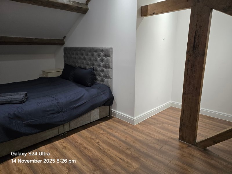 Bedroom with single bed, grey upholstered headboard, wooden beams and laminate flooring
