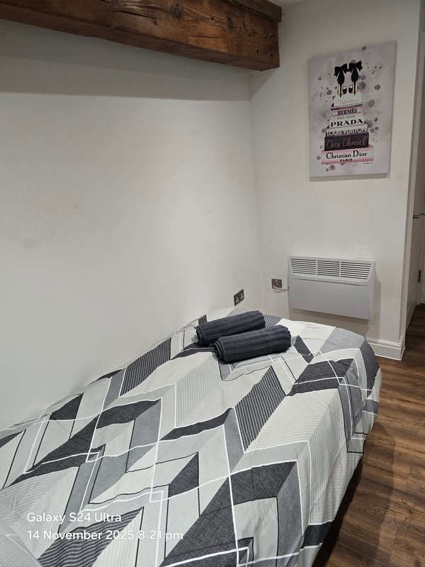 Bedroom with single bed, geometric patterned duvet, wooden beam and wall heater