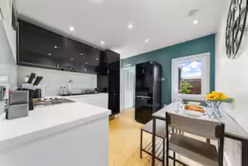 Modern kitchen with white countertops, black cabinets, teal accent wall and dining area