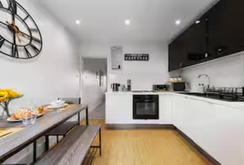 Modern kitchen and dining area with white cabinets, wooden floor, and wall clock