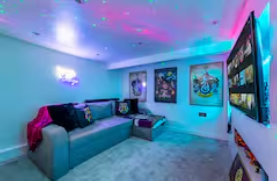 Modern gaming room with neon lighting, sofa, wall-mounted TV, and framed posters