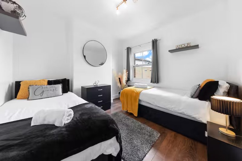 Modern twin bedroom with two single beds, circular mirror, window with curtains, wooden floor