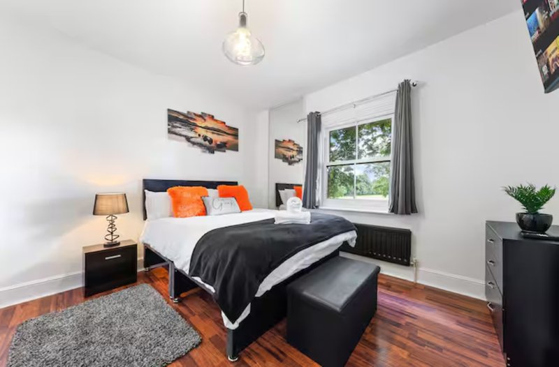 Bright bedroom with double bed, orange accents, wooden floor and large window