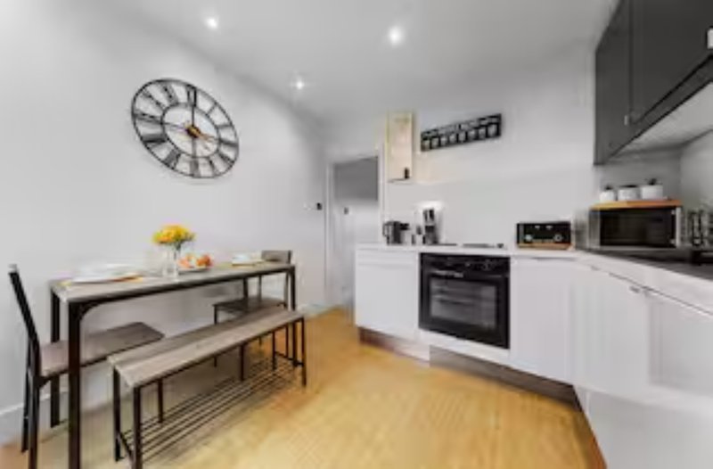 Modern kitchen with white cabinetry, dining table, wall clock and wooden flooring