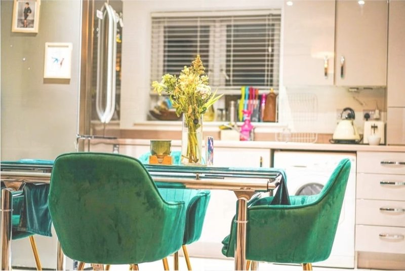 Modern kitchen and dining area with green chairs, wooden table, and yellow flowers in vase