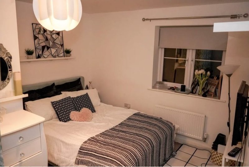 Small bedroom with single bed, white bedside table, pendant lamp, and window