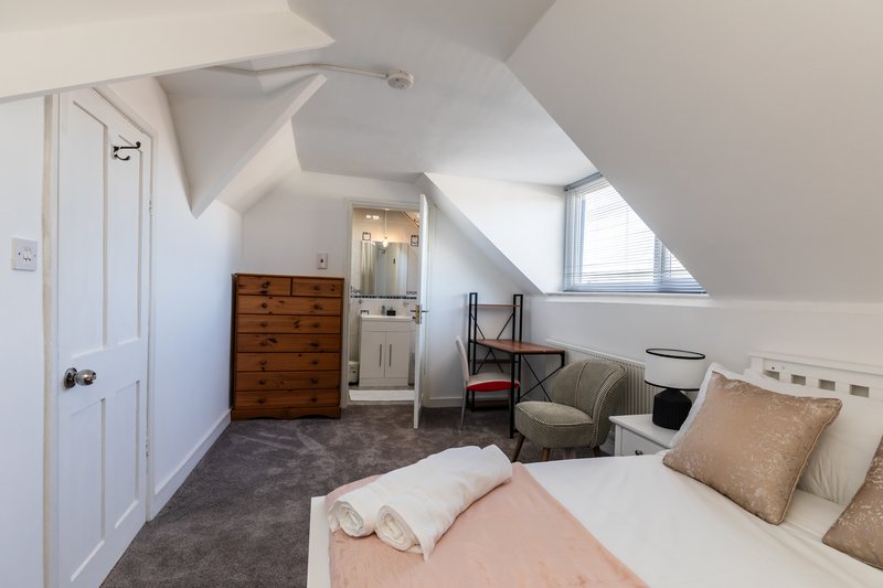 Attic bedroom with sloped ceiling, double bed, wooden chest of drawers, and seating area