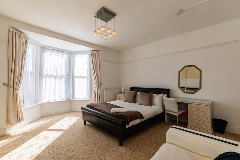 Spacious bedroom with double bed, bay windows with curtains, wooden furniture and ceiling light fixture