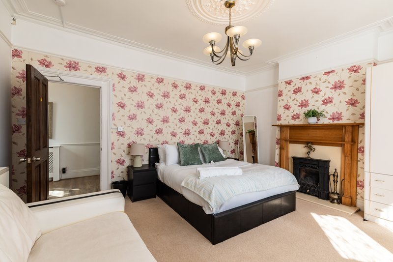 Spacious bedroom with double bed, floral wallpaper, fireplace, and ensuite bathroom
