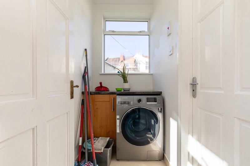 Compact laundry room with washing machine, wooden cabinet, window and cleaning supplies