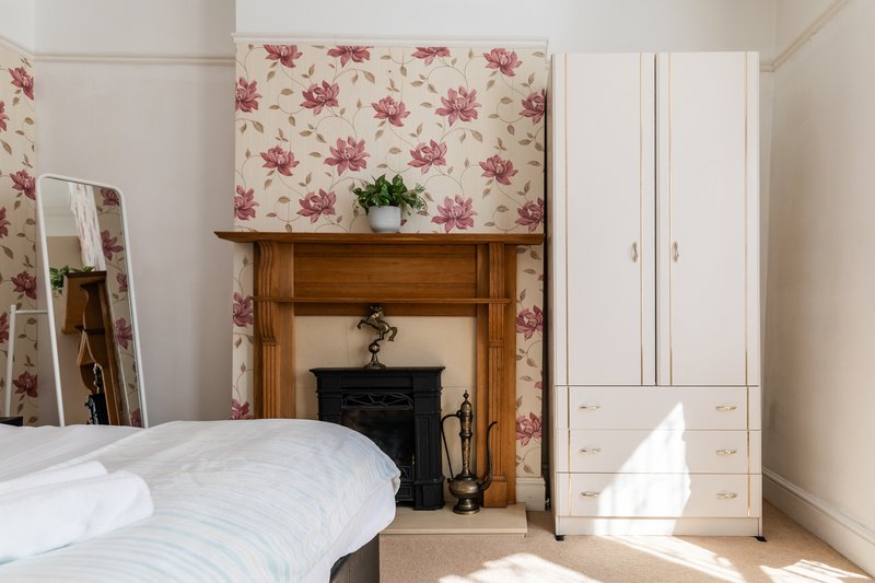 Bedroom with double bed, fireplace, floral wallpaper and white wardrobe