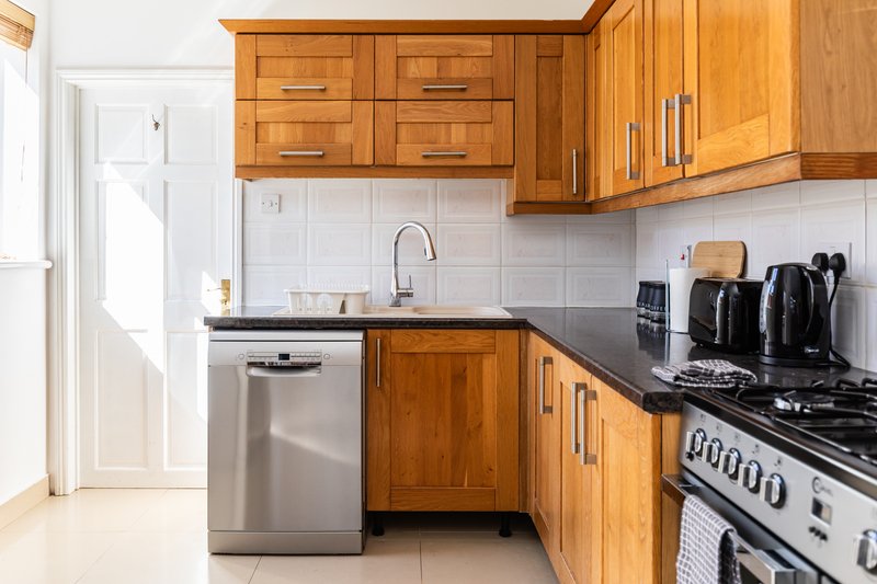 Kitchen with wooden cabinets, stainless steel appliances, white tile backsplash and black countertop