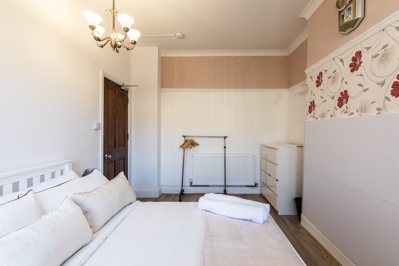 Bright bedroom with white bed, cream walls, floral wallpaper accent, chandelier and wooden door